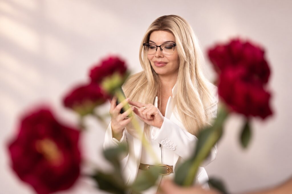 Ioana Dosinescu folosind telefonul printre flori roșii